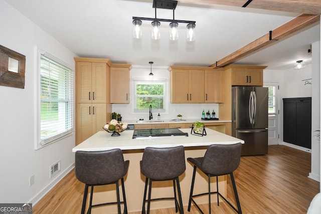 kitchen with light brown cabinetry, stainless steel appliances, decorative light fixtures, and light wood-type flooring