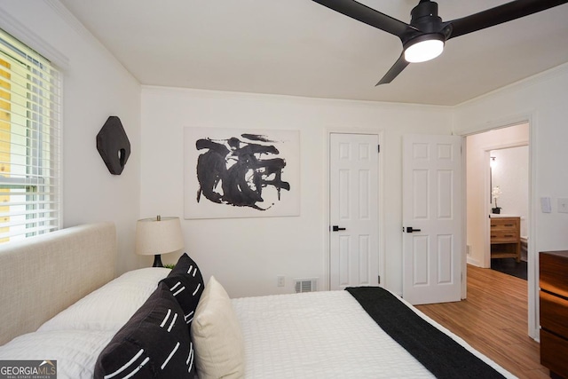 bedroom featuring multiple windows, hardwood / wood-style flooring, ceiling fan, and ornamental molding