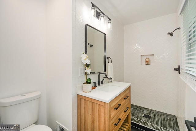 bathroom with a tile shower, vanity, and toilet