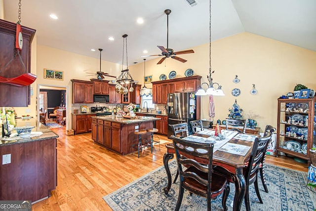 dining space featuring ceiling fan, sink, high vaulted ceiling, and light wood-type flooring