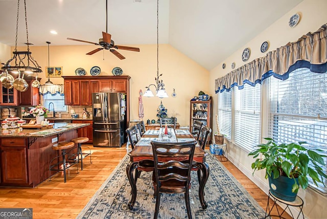 dining area with ceiling fan with notable chandelier, light hardwood / wood-style flooring, vaulted ceiling, and sink