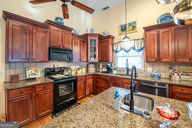 kitchen with decorative backsplash, light stone counters, sink, black appliances, and hanging light fixtures