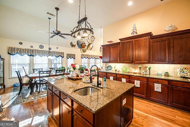 kitchen with light stone countertops, decorative backsplash, sink, hanging light fixtures, and an island with sink