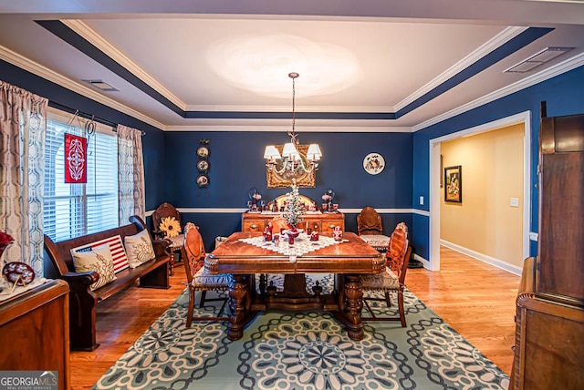 dining room featuring a notable chandelier, wood-type flooring, crown molding, and a tray ceiling