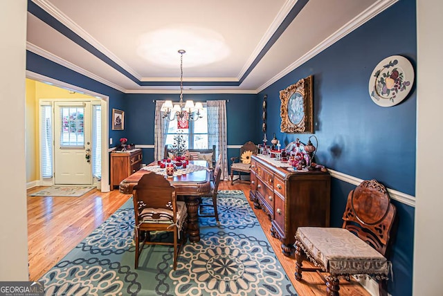 dining area featuring a chandelier, light wood-type flooring, a tray ceiling, and a wealth of natural light