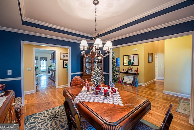 dining area featuring hardwood / wood-style flooring, a tray ceiling, crown molding, and a notable chandelier