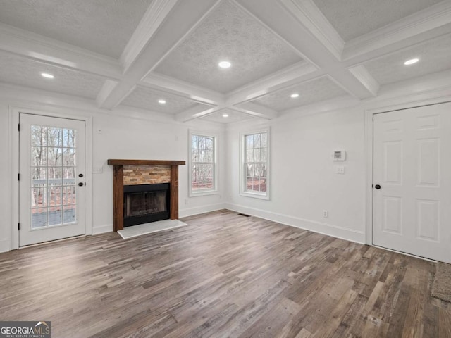 unfurnished living room featuring coffered ceiling, a stone fireplace, hardwood / wood-style flooring, a wealth of natural light, and beamed ceiling