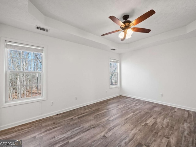 empty room with a textured ceiling, a tray ceiling, dark hardwood / wood-style floors, and ceiling fan