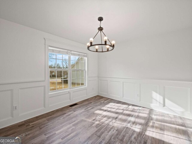 unfurnished dining area with wood-type flooring and a notable chandelier