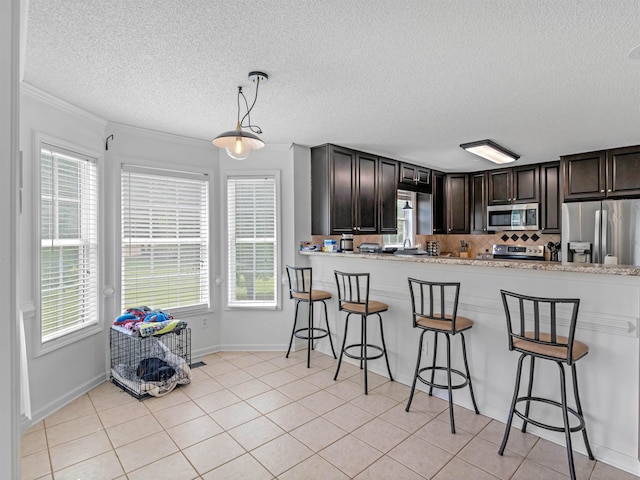 kitchen featuring kitchen peninsula, dark brown cabinets, stainless steel appliances, pendant lighting, and light tile patterned floors