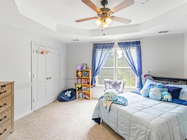 carpeted bedroom with a textured ceiling, a tray ceiling, ceiling fan, crown molding, and a closet