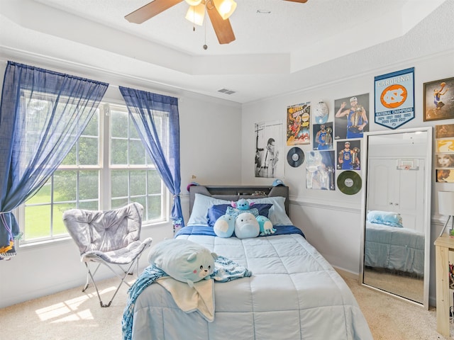 bedroom with crown molding, ceiling fan, a textured ceiling, a tray ceiling, and light colored carpet