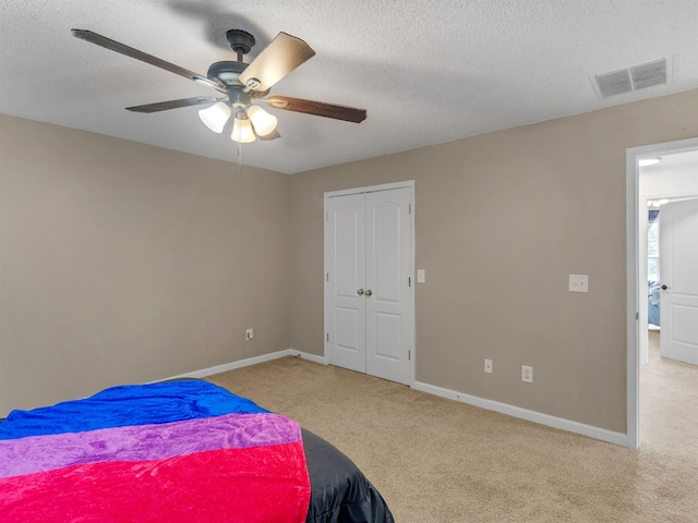 bedroom with a textured ceiling, light colored carpet, and ceiling fan