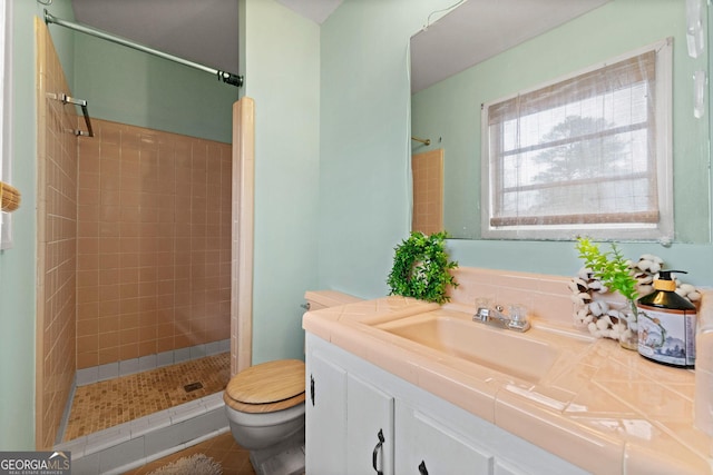 bathroom with toilet, a tile shower, vanity, and tile patterned floors