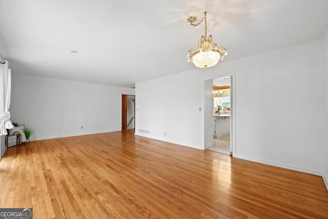 spare room featuring a chandelier and light hardwood / wood-style floors