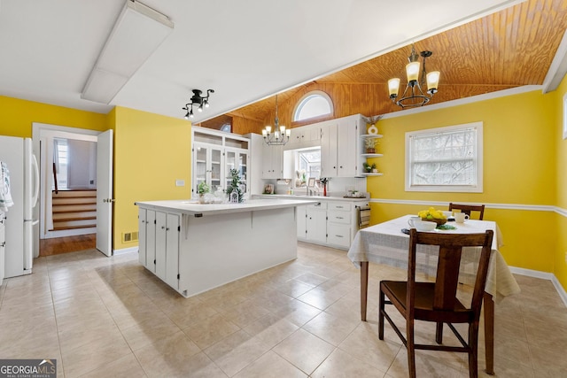 kitchen featuring vaulted ceiling, a kitchen island, decorative light fixtures, white fridge, and white cabinetry