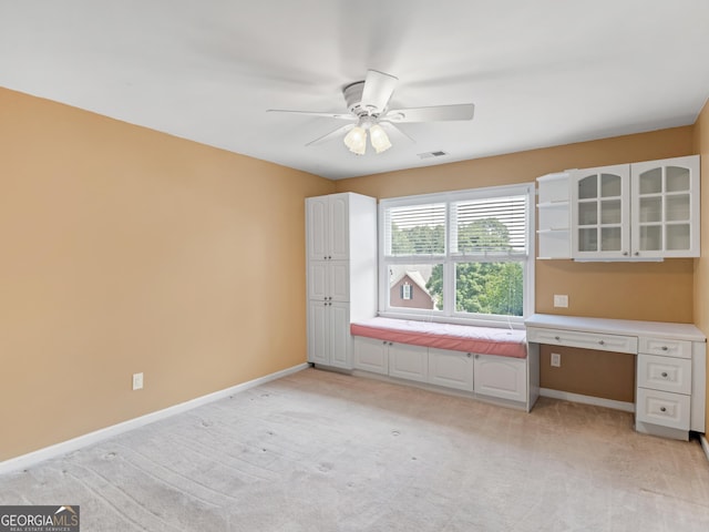 interior space featuring light carpet, ceiling fan, and built in desk