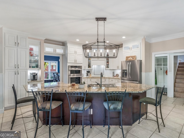 kitchen featuring white cabinets, a spacious island, light stone countertops, appliances with stainless steel finishes, and a breakfast bar area