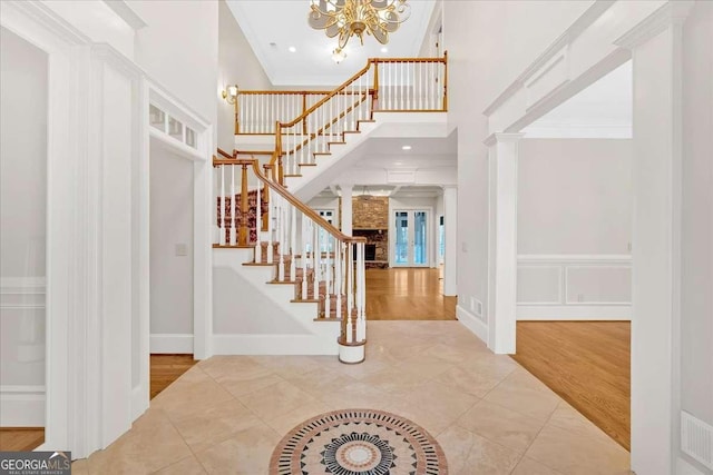 tiled foyer with decorative columns, crown molding, and an inviting chandelier