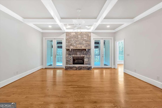 unfurnished living room with french doors, a stone fireplace, coffered ceiling, and beam ceiling