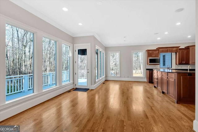 kitchen featuring sink, stainless steel microwave, ornamental molding, and light wood-type flooring