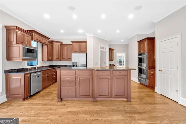 kitchen featuring appliances with stainless steel finishes, dark stone counters, ornamental molding, light hardwood / wood-style flooring, and a kitchen island