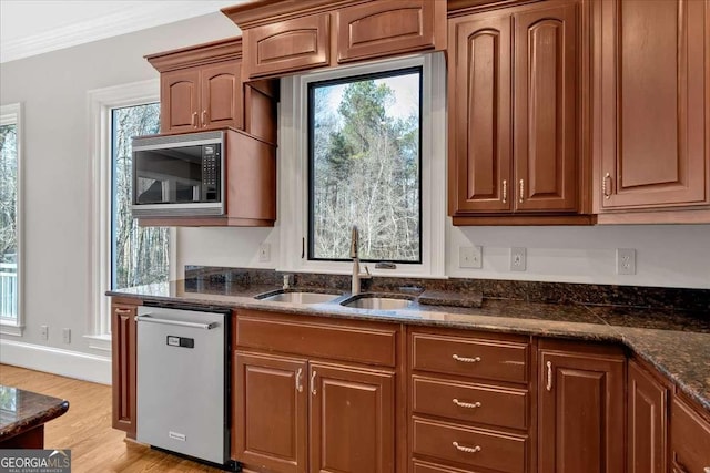 kitchen with dark stone counters, sink, light hardwood / wood-style flooring, ornamental molding, and appliances with stainless steel finishes