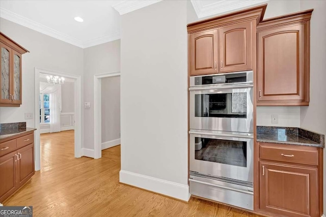 kitchen featuring ornamental molding, dark stone counters, stainless steel double oven, light hardwood / wood-style flooring, and a notable chandelier