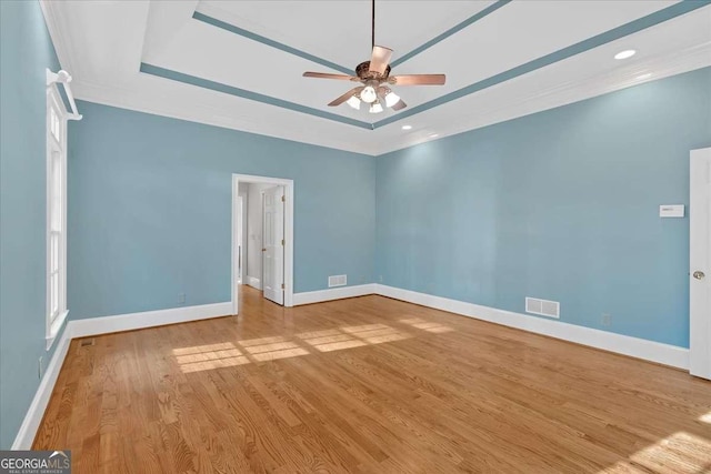 empty room with light wood-type flooring, a tray ceiling, ceiling fan, and crown molding