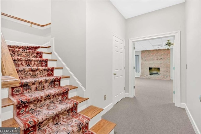 staircase with carpet flooring, ceiling fan, and a fireplace