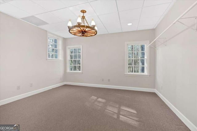 carpeted spare room featuring a chandelier and a drop ceiling