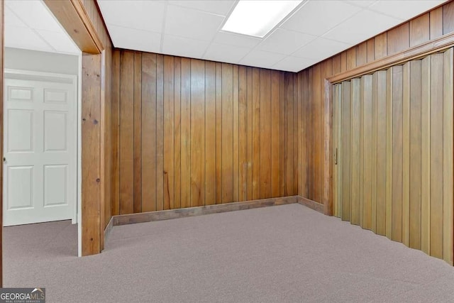 unfurnished room with carpet floors, a drop ceiling, and wooden walls