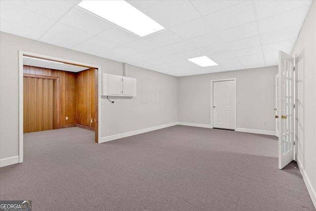 basement with a paneled ceiling, wood walls, and carpet floors