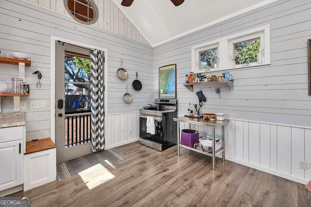 kitchen with lofted ceiling, wooden walls, electric range, light wood-type flooring, and white cabinetry