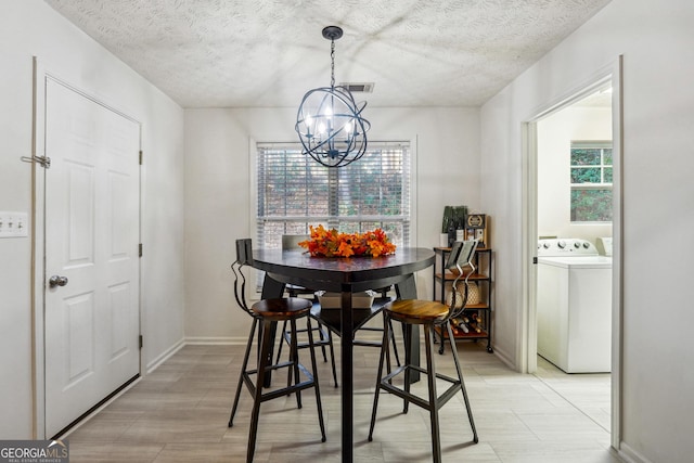 dining room featuring washer / clothes dryer, a healthy amount of sunlight, a textured ceiling, and a notable chandelier