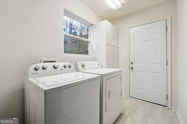 clothes washing area featuring cabinets, a textured ceiling, and washing machine and clothes dryer