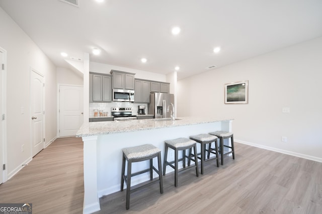 kitchen featuring a kitchen bar, stainless steel appliances, a center island with sink, light hardwood / wood-style flooring, and gray cabinets