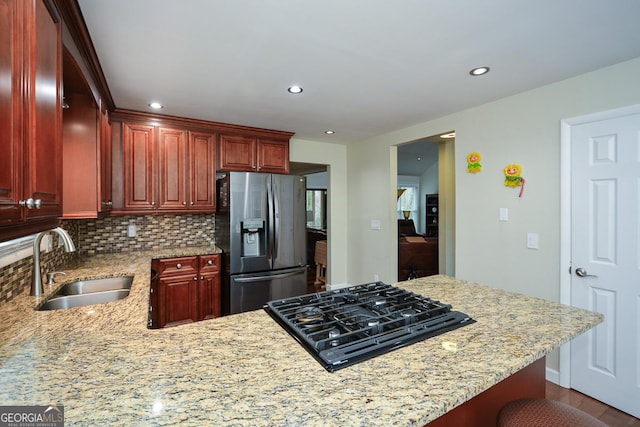 kitchen with light stone countertops, sink, black gas cooktop, stainless steel fridge, and a kitchen bar