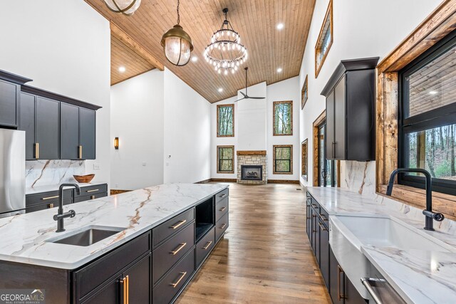 kitchen with decorative light fixtures, sink, wood ceiling, high vaulted ceiling, and an island with sink