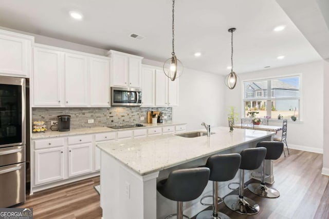 kitchen featuring white cabinets, sink, an island with sink, and black electric stovetop