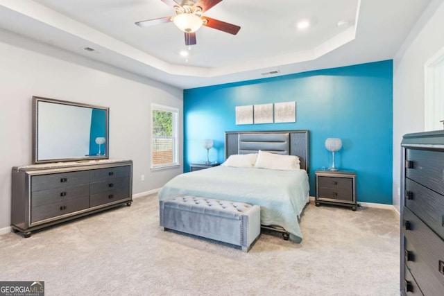 bedroom with light carpet, a tray ceiling, and ceiling fan