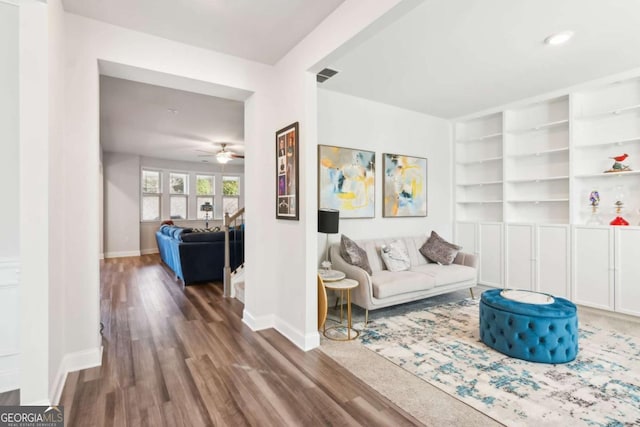 living room featuring built in shelves, dark hardwood / wood-style flooring, and ceiling fan