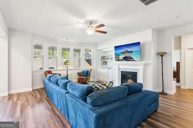 living room with built in shelves, hardwood / wood-style flooring, and ceiling fan