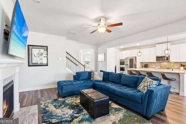 living room with ceiling fan, a fireplace, and light hardwood / wood-style flooring