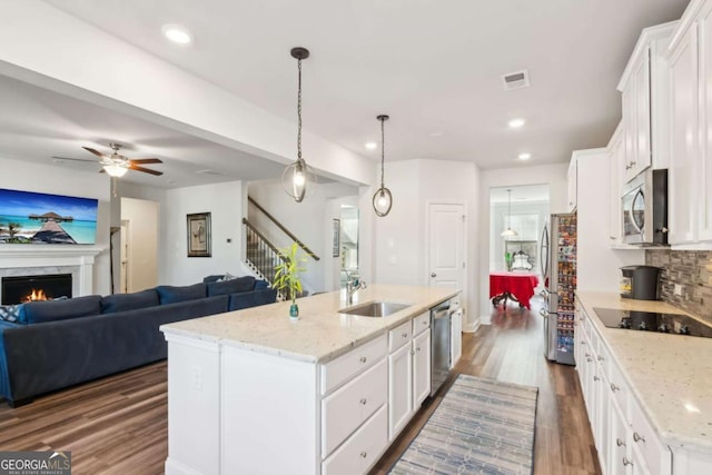 kitchen with white cabinetry, light stone countertops, hanging light fixtures, stainless steel appliances, and a kitchen island with sink