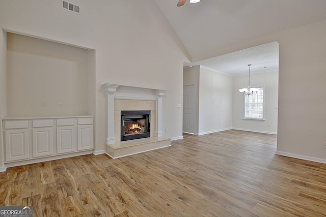 unfurnished living room with ceiling fan with notable chandelier, light wood-type flooring, a fireplace, and high vaulted ceiling