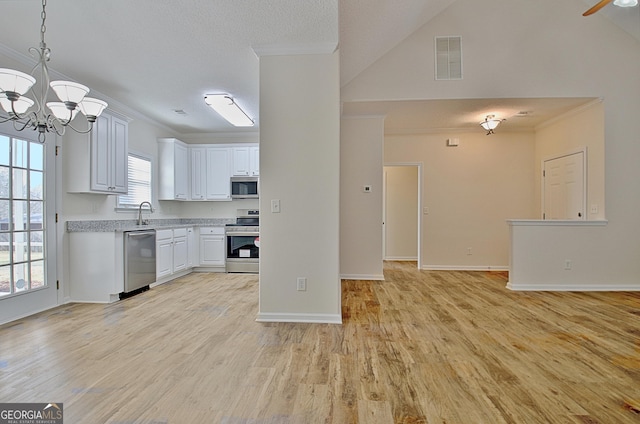 kitchen with appliances with stainless steel finishes, light wood-type flooring, a textured ceiling, decorative light fixtures, and white cabinetry