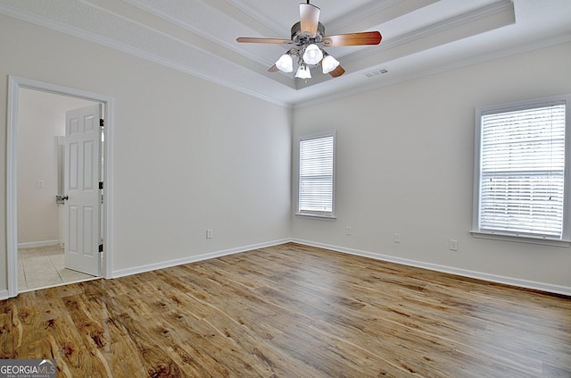 unfurnished room featuring light hardwood / wood-style floors, a raised ceiling, plenty of natural light, and ornamental molding