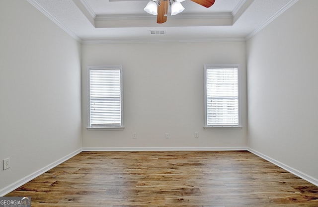 empty room featuring a raised ceiling, crown molding, hardwood / wood-style floors, and a healthy amount of sunlight