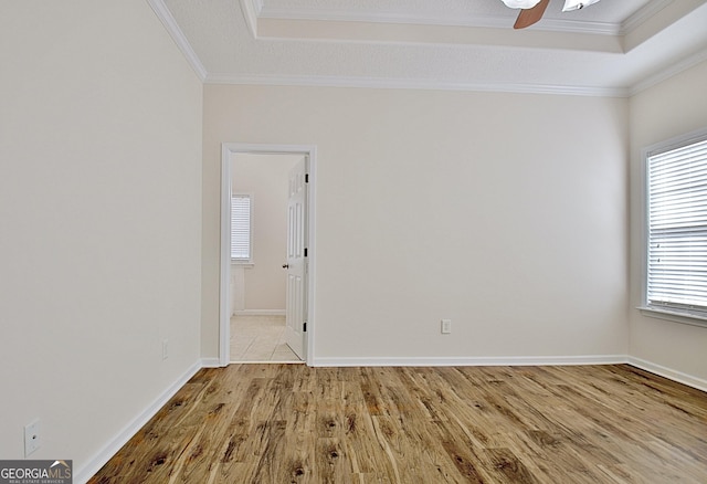 unfurnished room featuring ceiling fan, light hardwood / wood-style floors, a raised ceiling, and ornamental molding